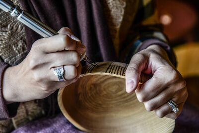 Person hand-carving intricate designs onto a wooden bowl using a precision tool